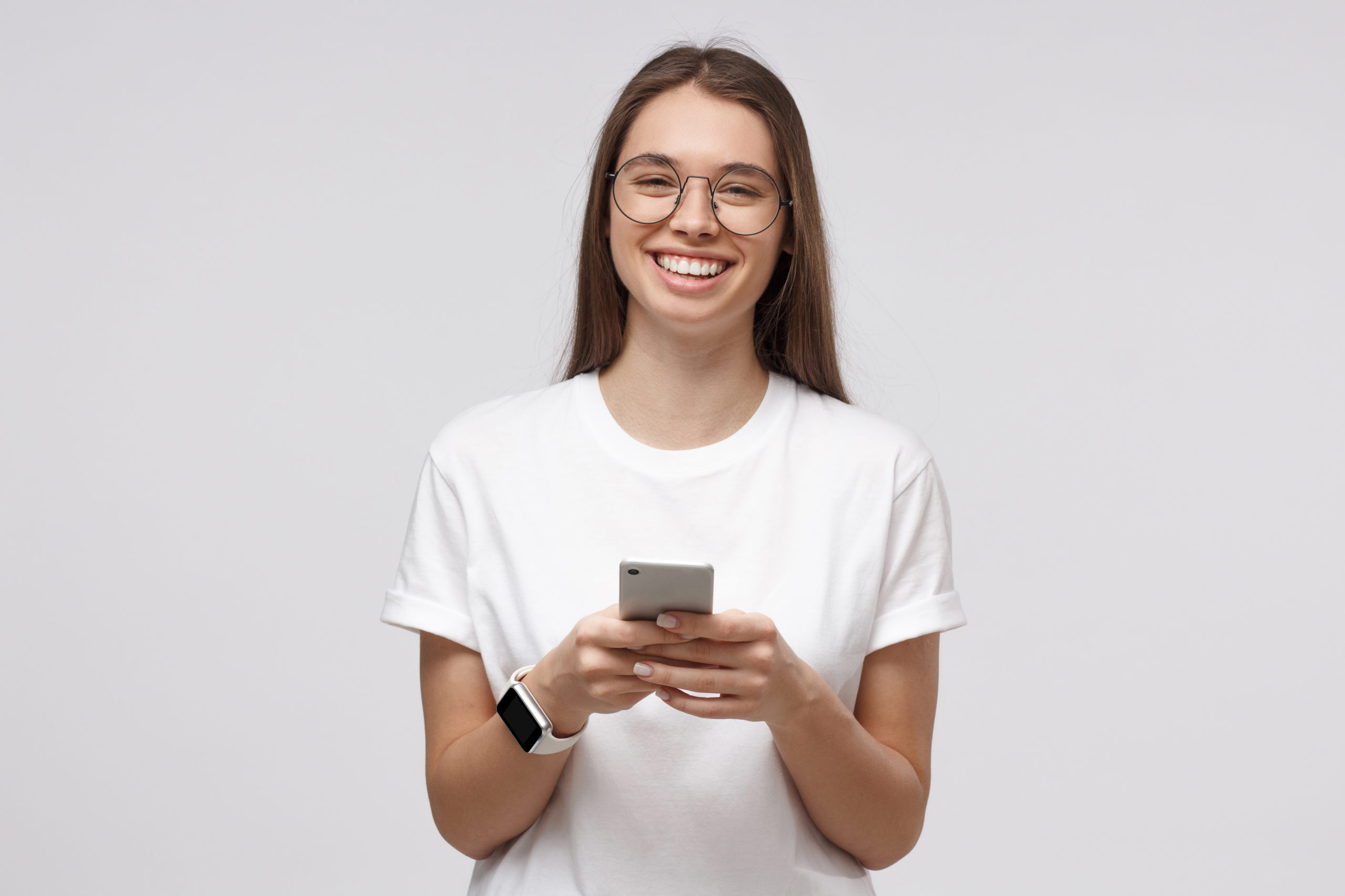 Beautiful girl in transparent glasses exchanging mesages with smart phone, isolated on gray background